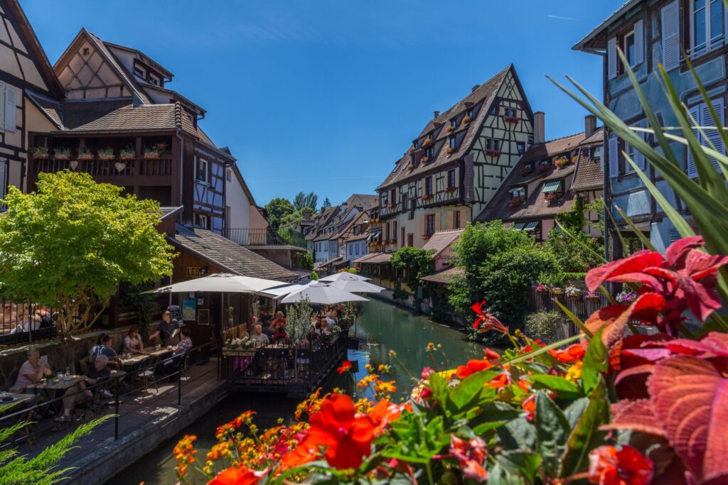 pexels-photo-28572721-28572721 Picturesque view of a riverside cafe in Colmar with vibrant flowers and traditional architecture.
